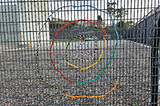 multi coloured threads woven into a swirl shape on a wire fence