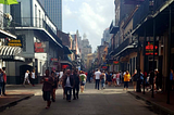 People walking down Bourbon Street surrounded by balconies neon signs and the echo of jazz in the heart of New Orleans