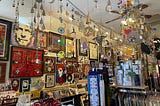 The interior of a shop, with metal decorations hanging from the ceiling, pieces of artwork on the walls, and various art pieces all around.