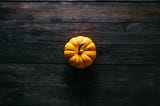 A photo from above of a small orange pumpkin on a dark brown wooden table top