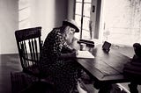 Black and white photo of woman sitting alone at table writing