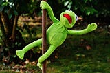 Kermit the frog on a pole. He is doing a pole dance move.