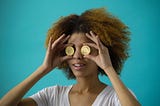 A woman holds up two bitcoins in front of her eyes so she cannot see.
