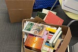 Boxes filled with books sitting on a floor and one on a chair