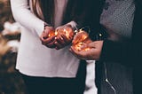 Close-up photo of two person holding lighted string lights.