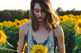 woman in field looking down at sunflower