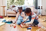 Two adorable black children playing with blocks in their Etobicoke, Toronto Home playing with blocks with their father in the background sleeping on the couch. Shawnette Thompson — Toronto’s NARM Therapist — Childhood trauma — CPTSD — complex trauma