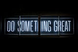 Neon sign lit up with “Do Something Great” against a black backdrop.