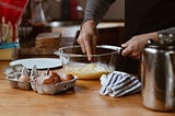 A person stirs a yellow substance in a clear bowl. Egg shells are in a carton on the counter. Mom’s Lemon Meringue Pie by Jim Latham | Photo by Sincerely Media on Unsplash