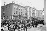 Photograph shows an Emancipation Day parade on Main Street, Richmond, Virginia. The building in the back is 1000 Main Street.
