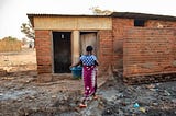 A Malawian woman makes her way through a cluttered pathway on her way to a inadequate toilet facility at a health center.