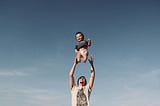 Blue sky back ground. Happy baby in mid-air as a man throws him up to catch him again.