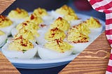 Deviled eggs on a white plate, against a background of a wooden table with a white and red checked tablecloth