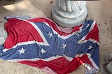 A Confederate flag towel draped casually over the side walk at an office building.