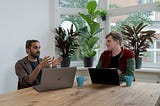Two men sit at a table talking to each other
