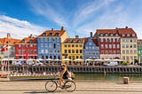 A woman biking along the river in Copenhagen, Denmark, on a sunny day.
