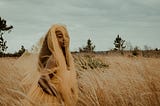 Black woman in a yellow veil walking through a wheat field.