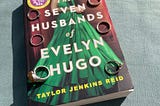 The book ‘The Seven Husbands of Evelyn Hugo’ by Taylor Jenkins Reid, with 7 rings placed on the cover