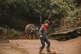 A Hmong boy plays soccer in his village near Sapa, Vietnam, while a water buffalo walks behind him.