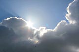 The bright, shining edge of a cloud is illuminated by the sun behind it, creating a glowing outline against the sky.