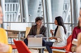 Photo of two coworkers sitting at a table talking