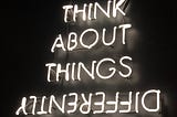 Photo shows a neon sign that says “Think about things differently.” The word differently is upside down.