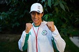 An image of Algerian champion women’s amateur boxer Imane Khelif smiling with her fists up.