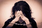 A dark-haired woman leaning her against her handcuffed and clasped hands.