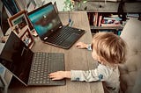 Baby sitting at a desk in front of two laptops