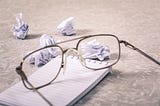 glasses on a note pad with bunched up paper balls thrown around