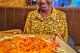 A beautiful Ugandan lady holding a carton of pizza