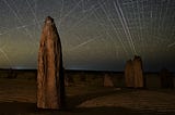 Dozens of satellite trails streak across a star-filled sky over the Pinnacles limestone formations in Western Australia, captured in a long-exposure image.