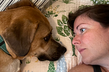 A woman and her dog stare at each other in bed.