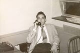 1950s man in his early 20s on the phone in a stark office