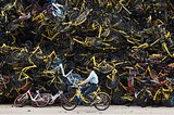 A worker rides a shared bicycle past a huge pile of unused shared bikes in a vacant lot in Xiamen, Fujian province, China, on December 13, 2017.