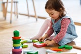 little baby girl playing with wooden toy blocks on floor at Kindergarten. Naperville Kindergarten