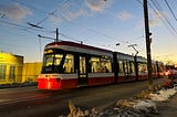 Red and white streetcar against blue sky with wispy white clouds at dusk