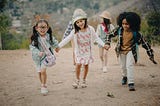 Several white children and one black girl holding hands and walking up a dirt hill.