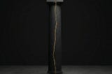 A broken black structural pillar rejoined with a single seam of gold, representing scar tissue as the authority behind Sovereign Leadership Architecture.