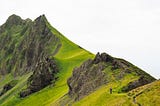 Craig stands on a grassy ridgeline that rises ahead of him.