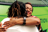 Two Black women hug in front of the Roadtrip Nation green RV.