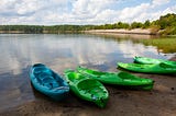 Five kayaks sitting along the bank of Jordan Lake, the trees and clouds outstretched along the horizon.