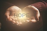 Outstretched hands cupping the word HOPE, with light radiating from the word.