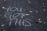 The words “You got this” written in white chalk on an black, asphalt drive.