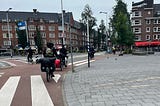 Four bikes ride through the streets of Amsterdam. One has a dog trailer attached.