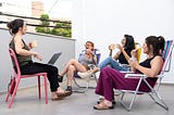 A group of 4 women sat on chairs, talking and drinking