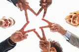 A diverse group of five people in professional attire are pictured from below as they hold out their fingers in V shapes and touch them together to form a star.
