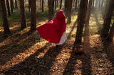 Woman in a handmaid’s tale style red robe running through a forest