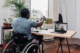 A man in a wheelchair using a handcycle exercising to a Kakana crosscycle class on his computer.