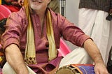 Me, sitting cross-legged with fancy clothes & a drum from India